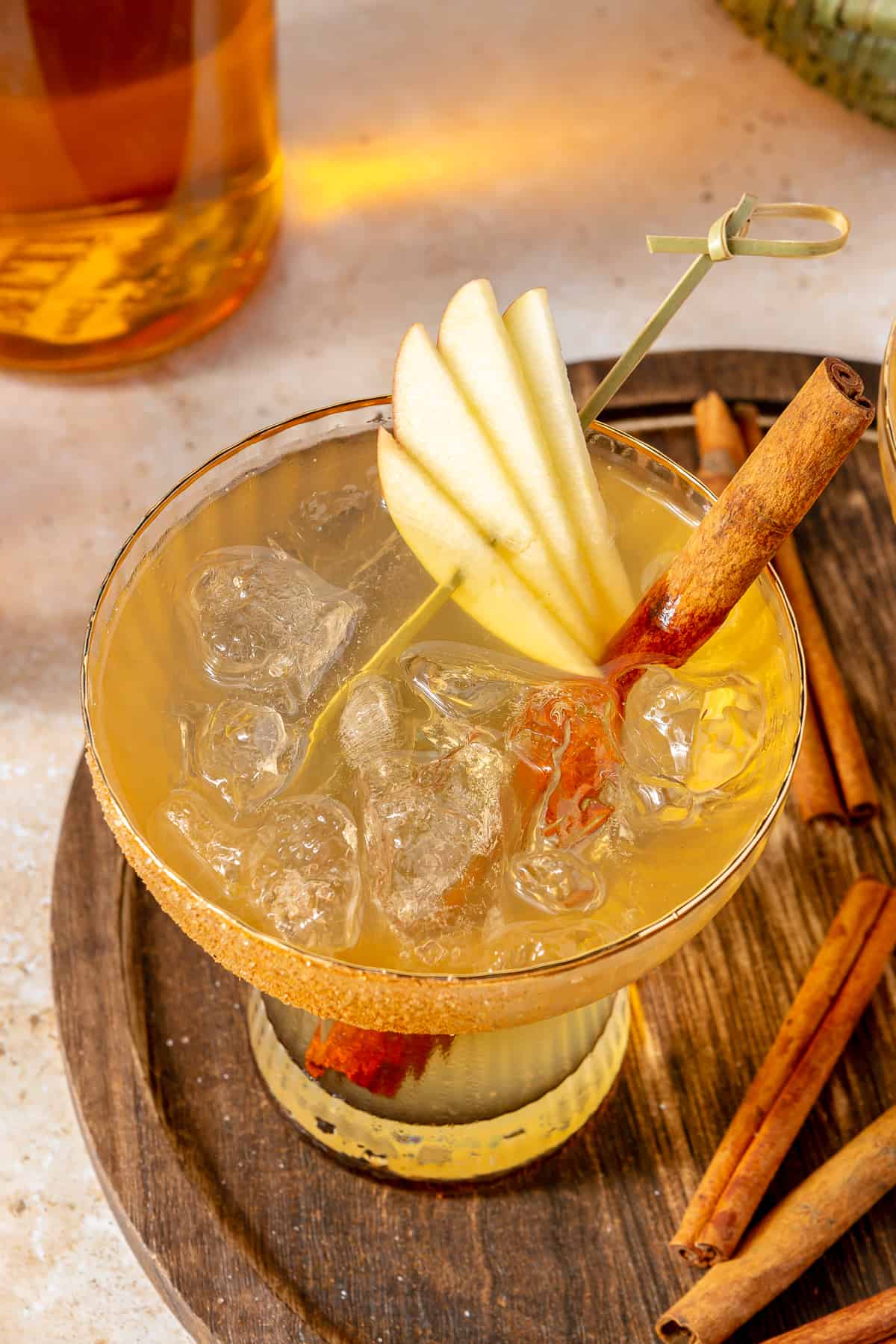 Stemless margarita glass with apple cider margarita garnished with slices of apple on a wooden board. 