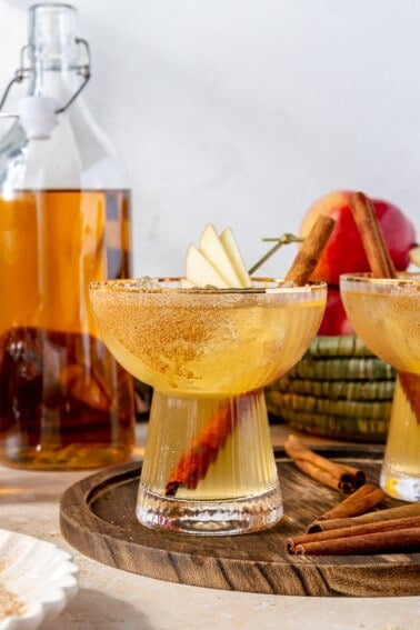 Glass filled with apple cider margarita garnished with slices of apples and cinnamon stick.