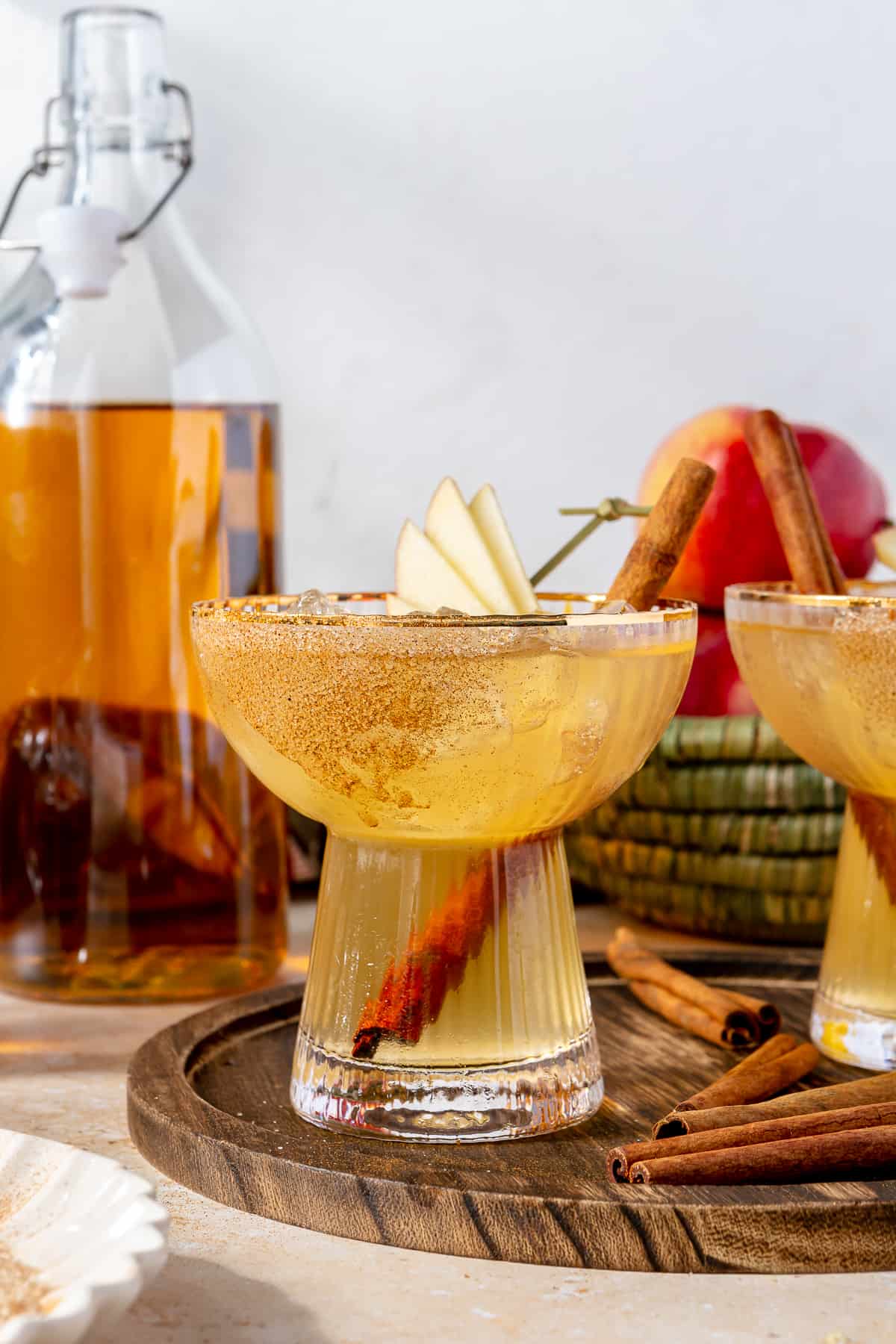 Glass filled with apple cider margarita garnished with slices of apples and cinnamon stick. 