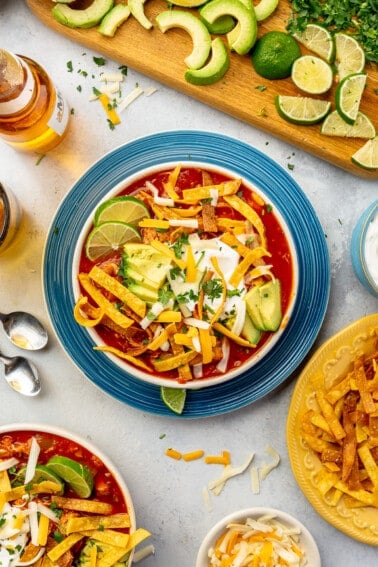 Bowl of chicken tortilla soup with toppings surrounding.
