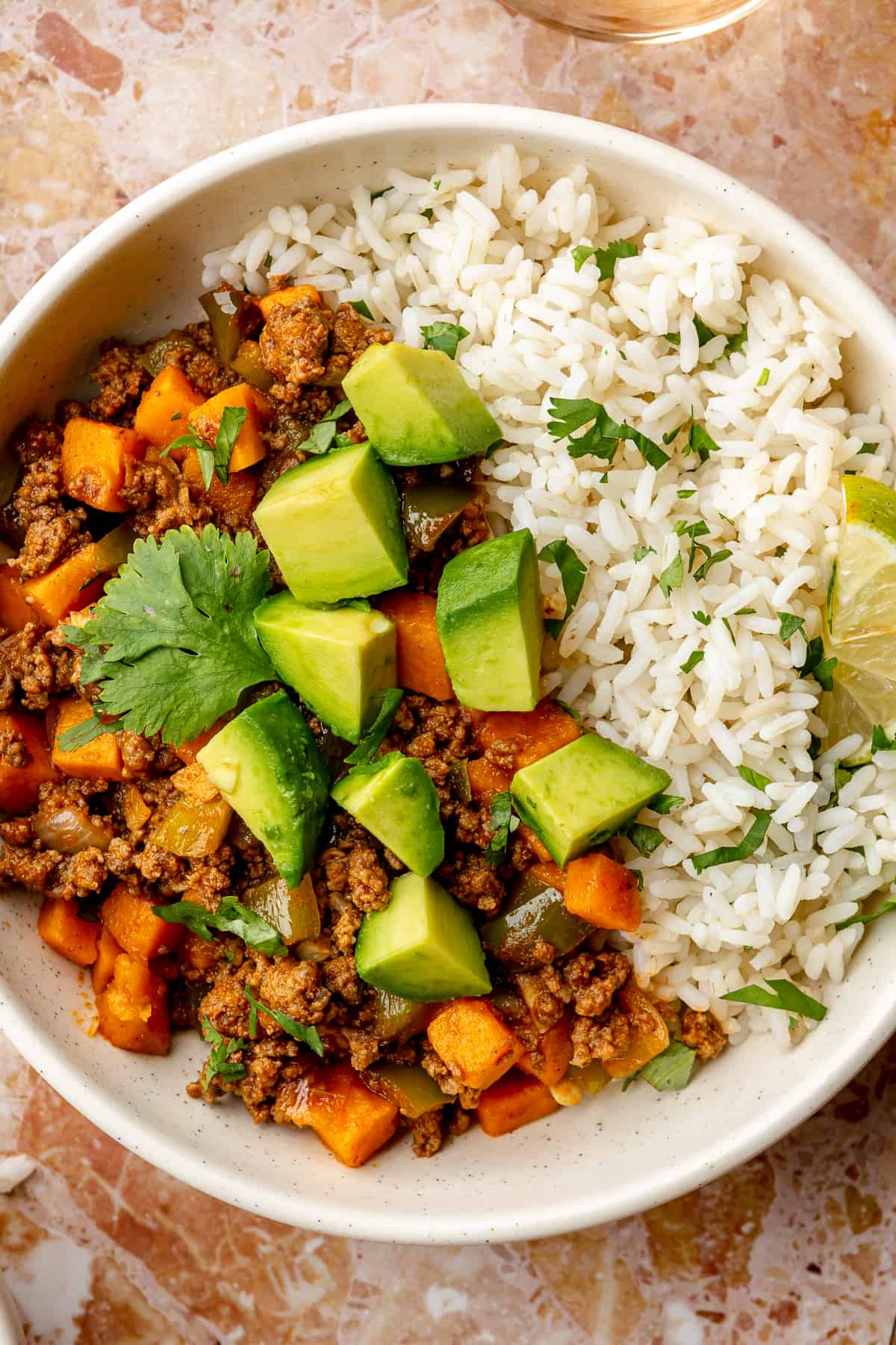 Up close image of sweet potato and ground beef picadillo over rice and topped with diced avocado. 