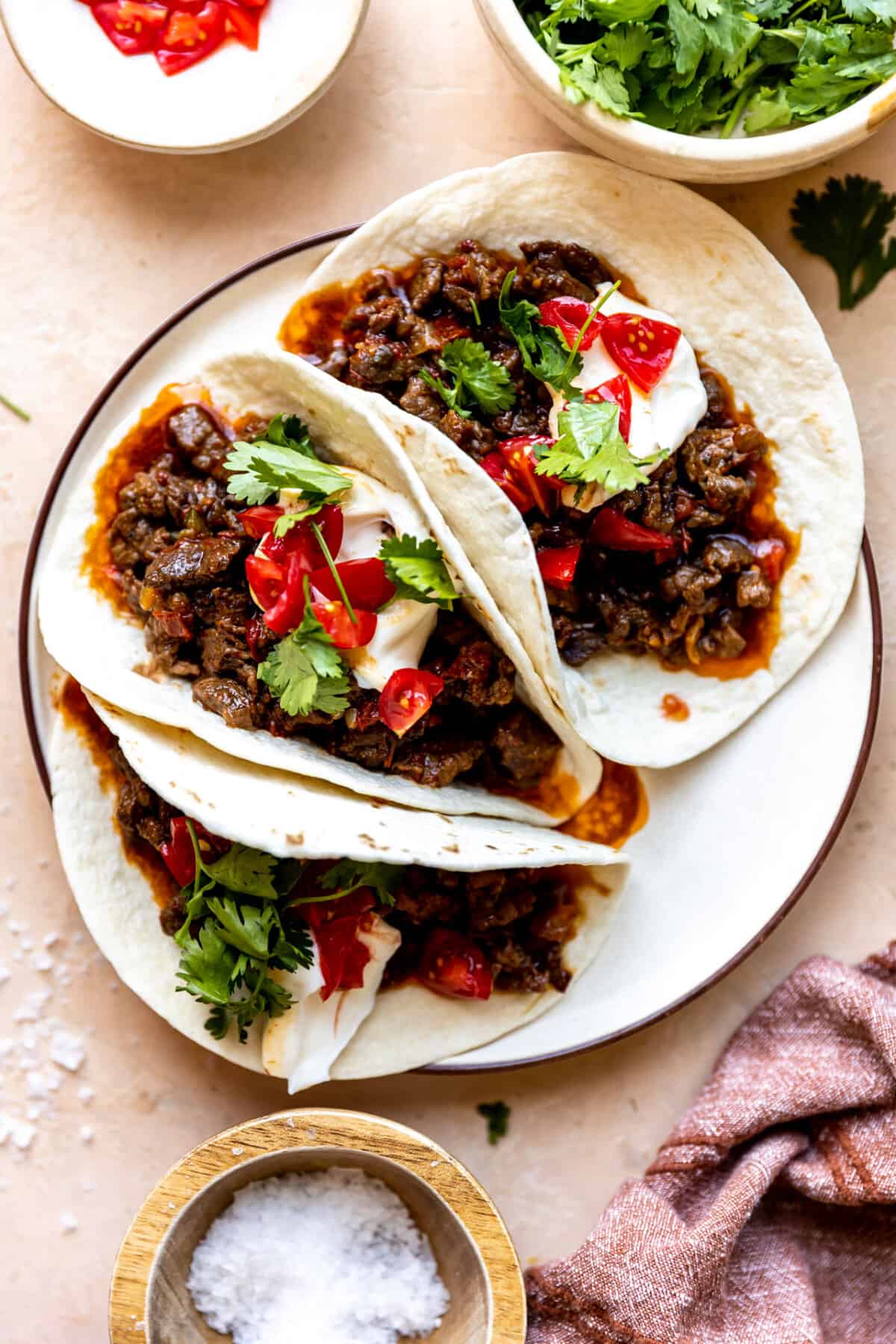 Plate of flour tortillas filled with carne cicada topped with sour cream, tomatoes and cilantro. 
