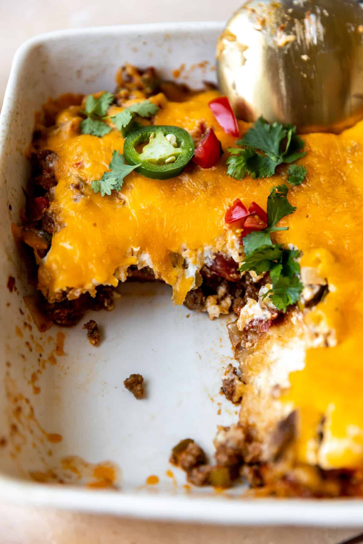 John Wayne Casserole in a baking dish after serving showing layers of biscuit, meat and cheese with tomatoes. 