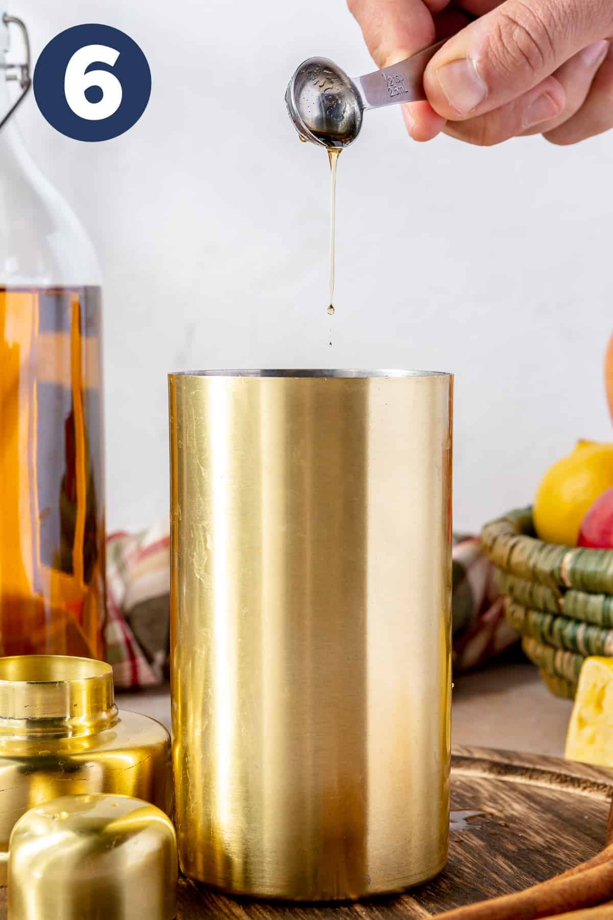 Measuring spoon dripping maple syrup into a cocktail shaker. 