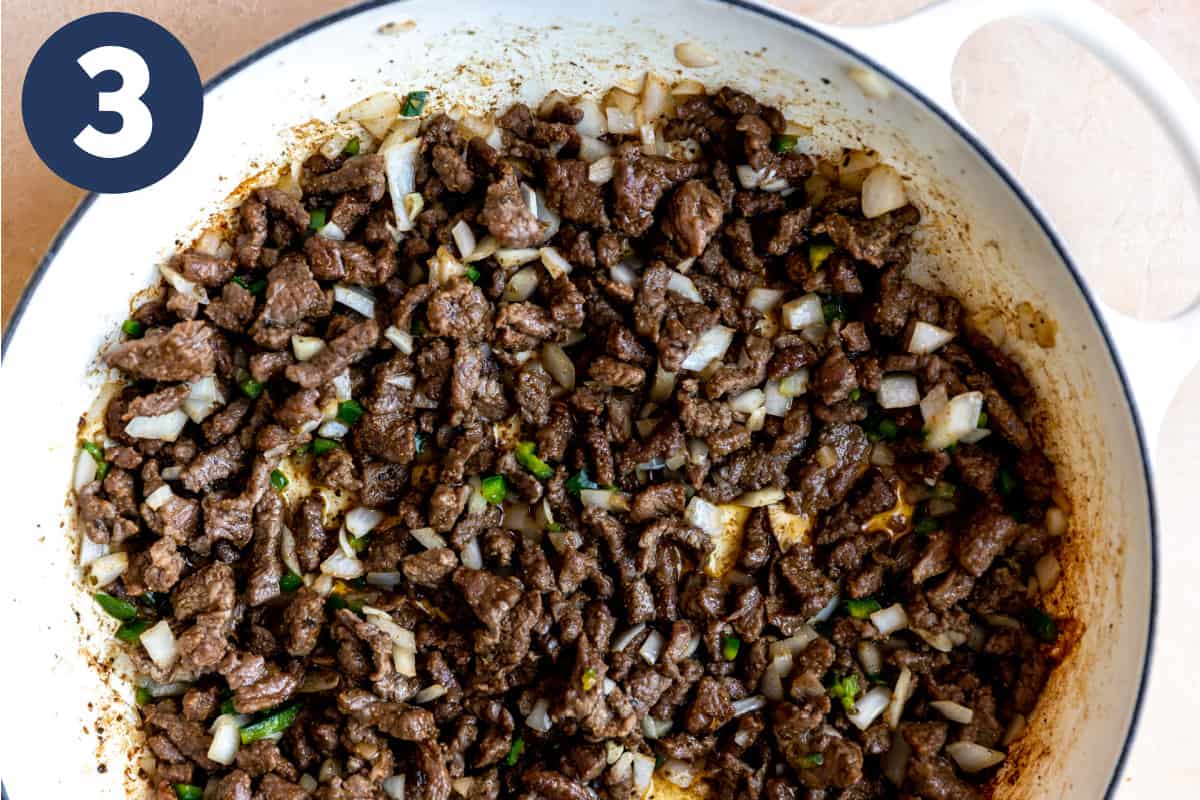 White skillet with chopped chuck roast being cooked with onions and peppers to make carne picada.