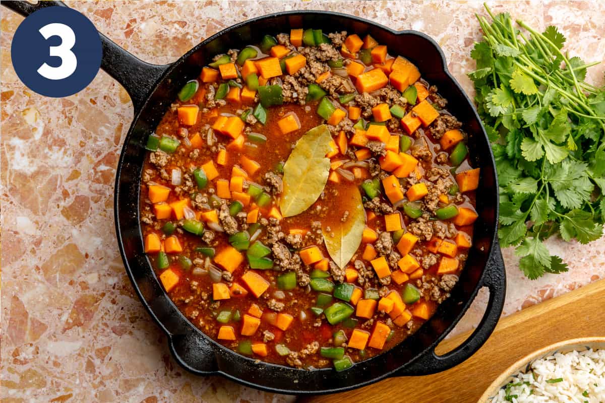 Broth and tomato sauce added to beef and sweet potato skillet meal, topped with bay leaves. 