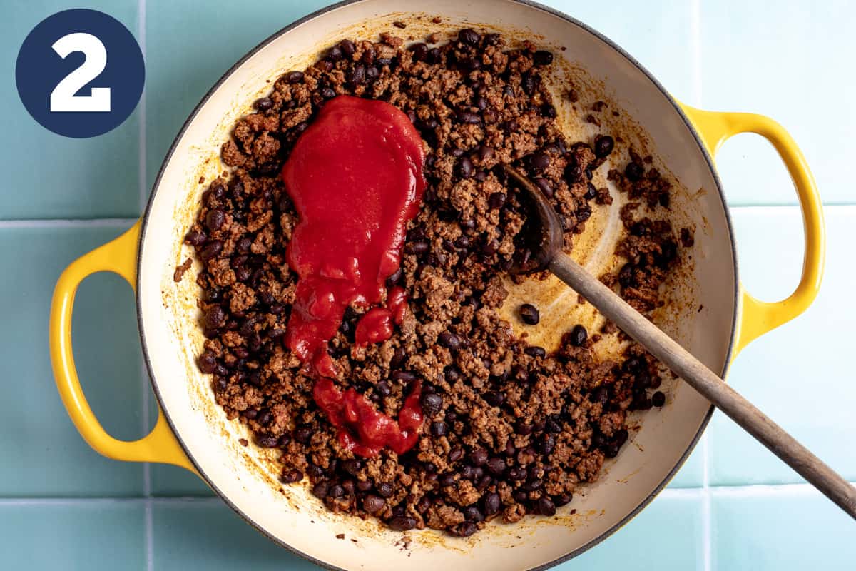 Cooked ground beef seasoned with taco seasoning and tomato sauce being added.