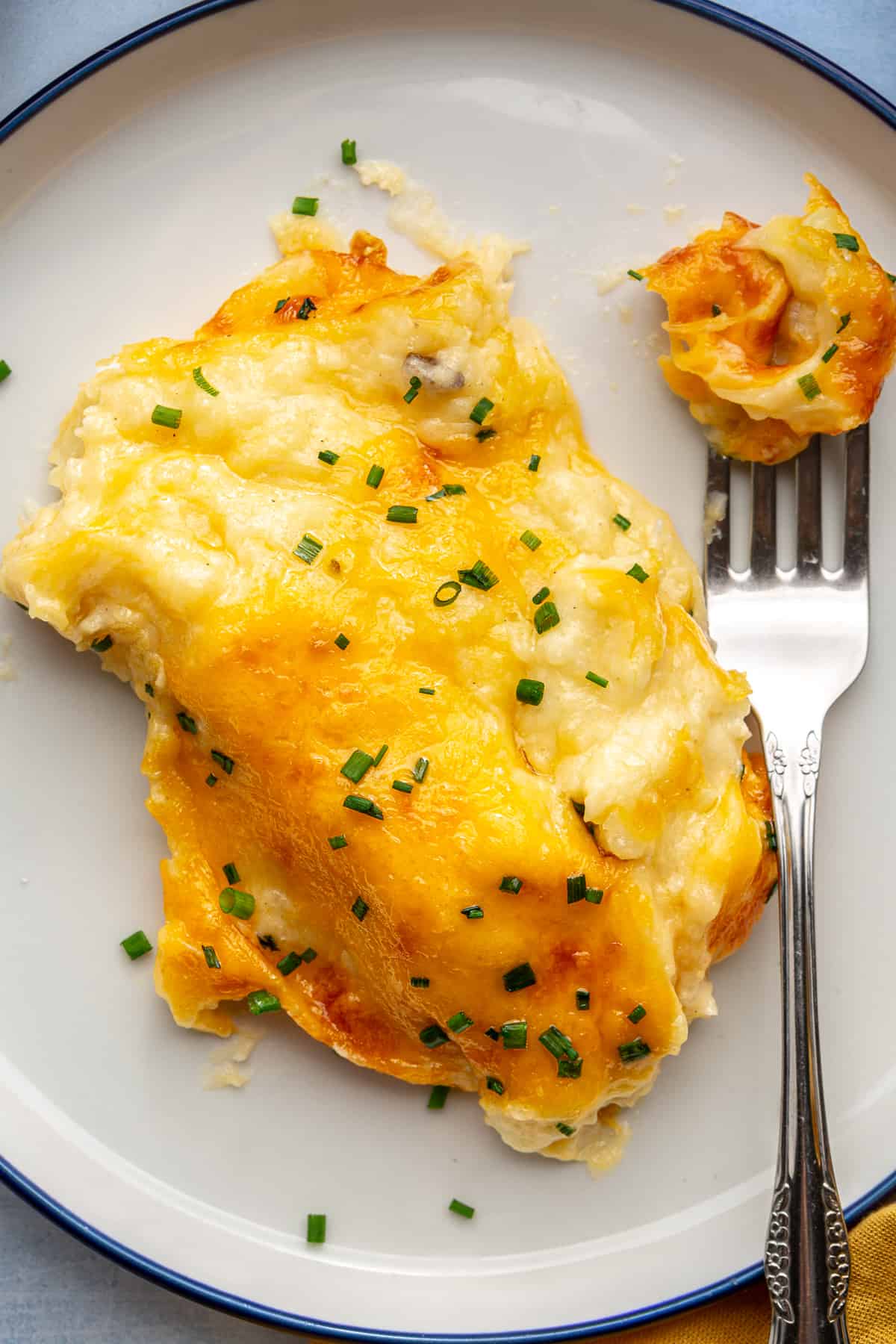 Cheesy mashed potatoes served on a plate with a fork. 