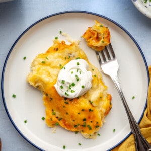 Plate with cheesy mashed potatoes topped with sour cream and chives.