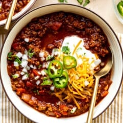 Bowl of ground beef Texas Chili topped with sour cream, sliced jalapeños, and shredded cheese.