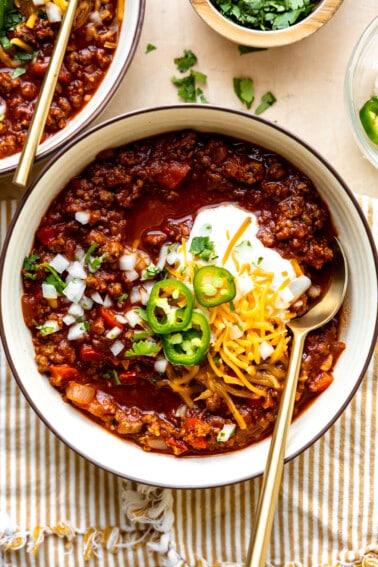 Bowl of ground beef Texas Chili topped with sour cream, sliced jalapeños, and shredded cheese.