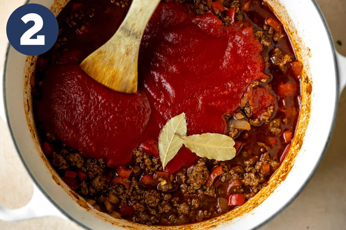 Tomato sauce, broth, and bay leaves added to a dutch oven to make a Texas style chili. 