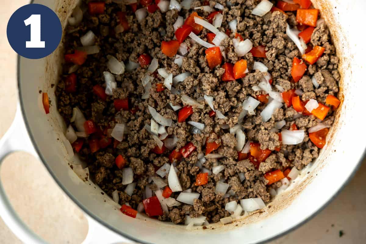 Cooked ground beef, white onion, and red bell pepper in a dutch oven. 