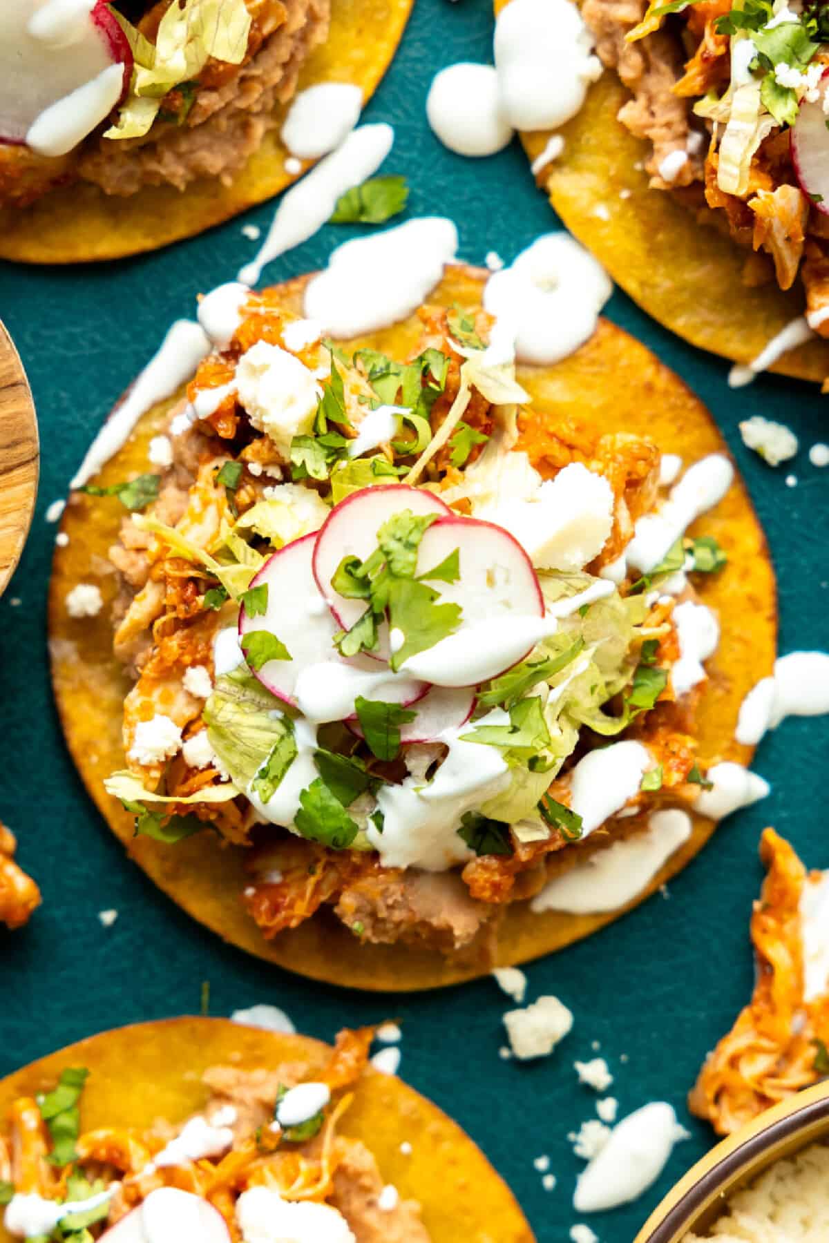 Overhead image of a tostada topped with beans, chicken, cheese, lettuce, radishes and drizzled with crema. 