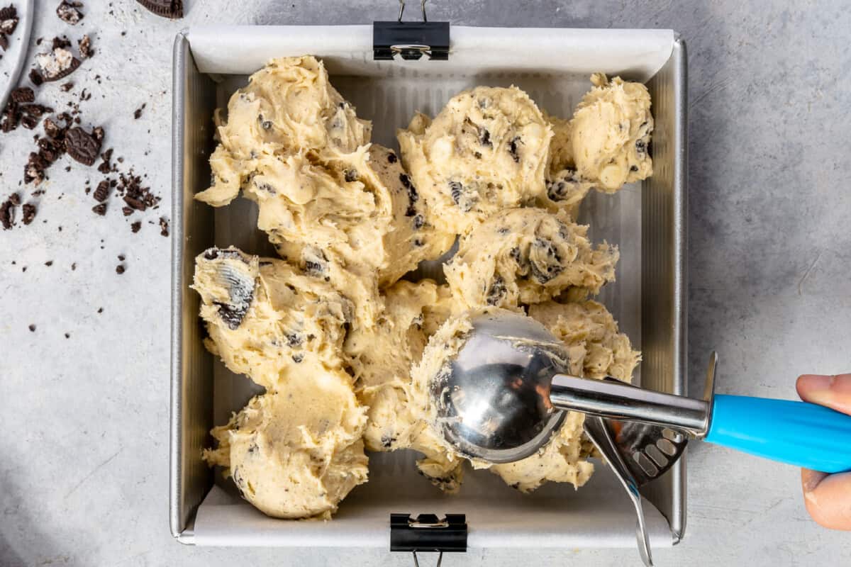 Oreo bar dough being spooned into a square baking pan.