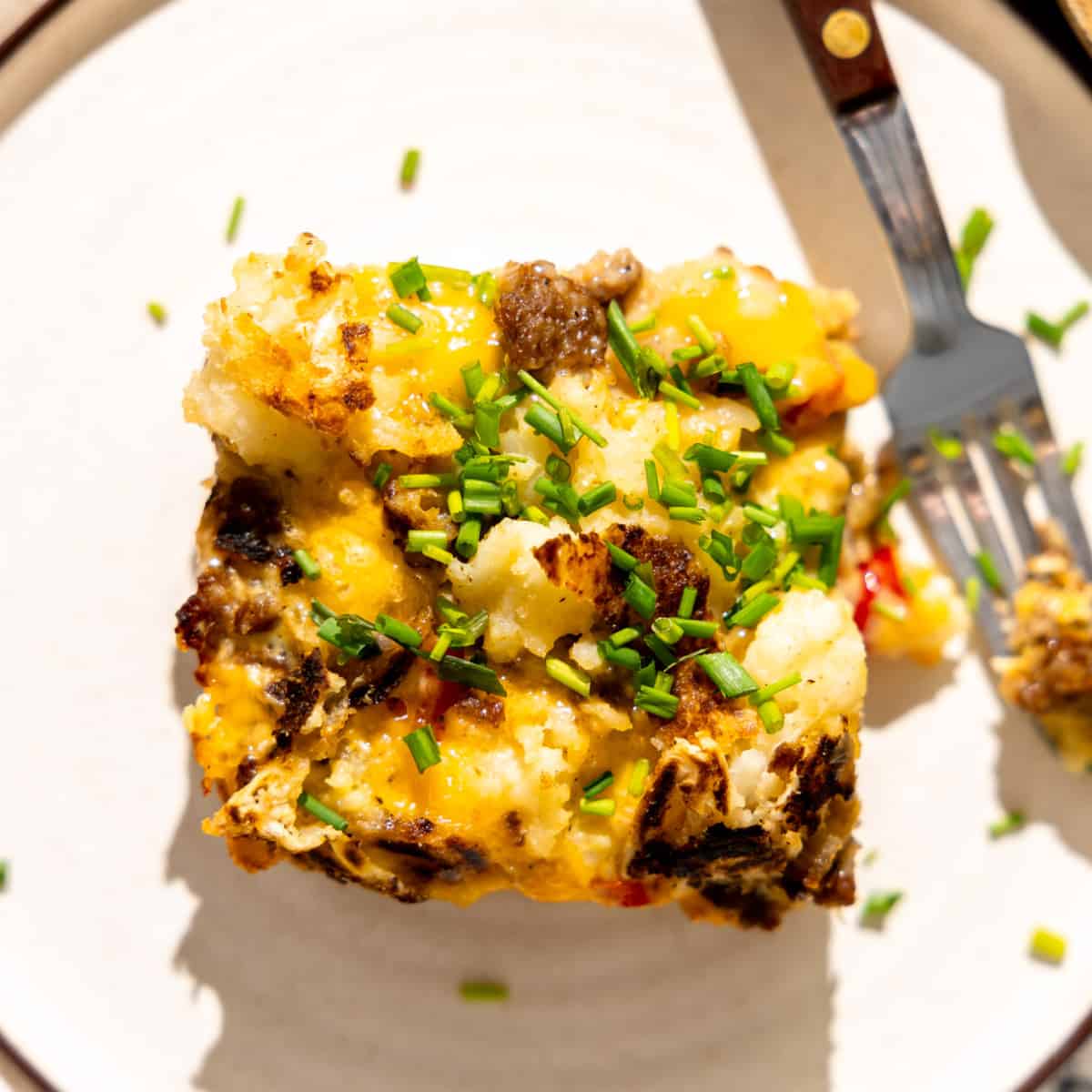 Slice of hashbrown casserole on a plate with a fork. 