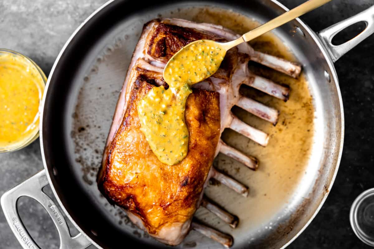 Spooning dijon sauce over the top of a rack of lamb. 