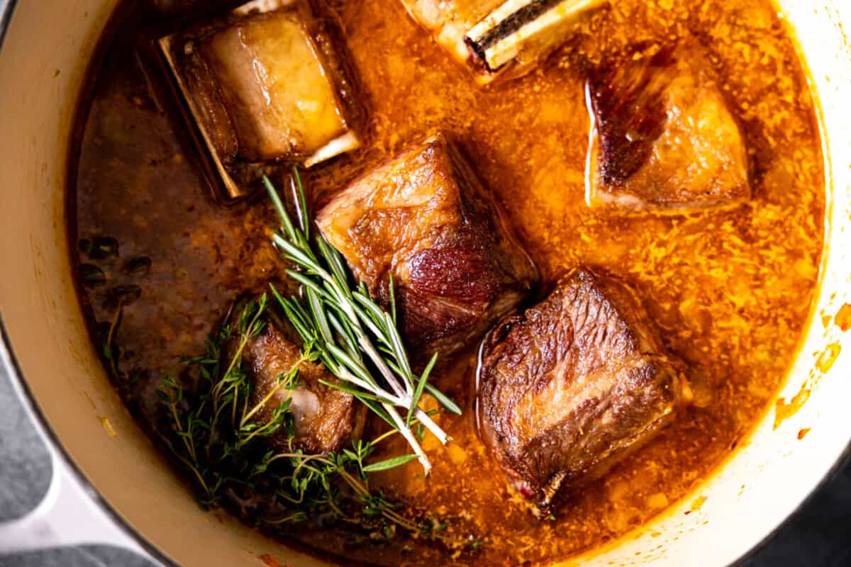 Short ribs in pan with sauce and fresh herbs.