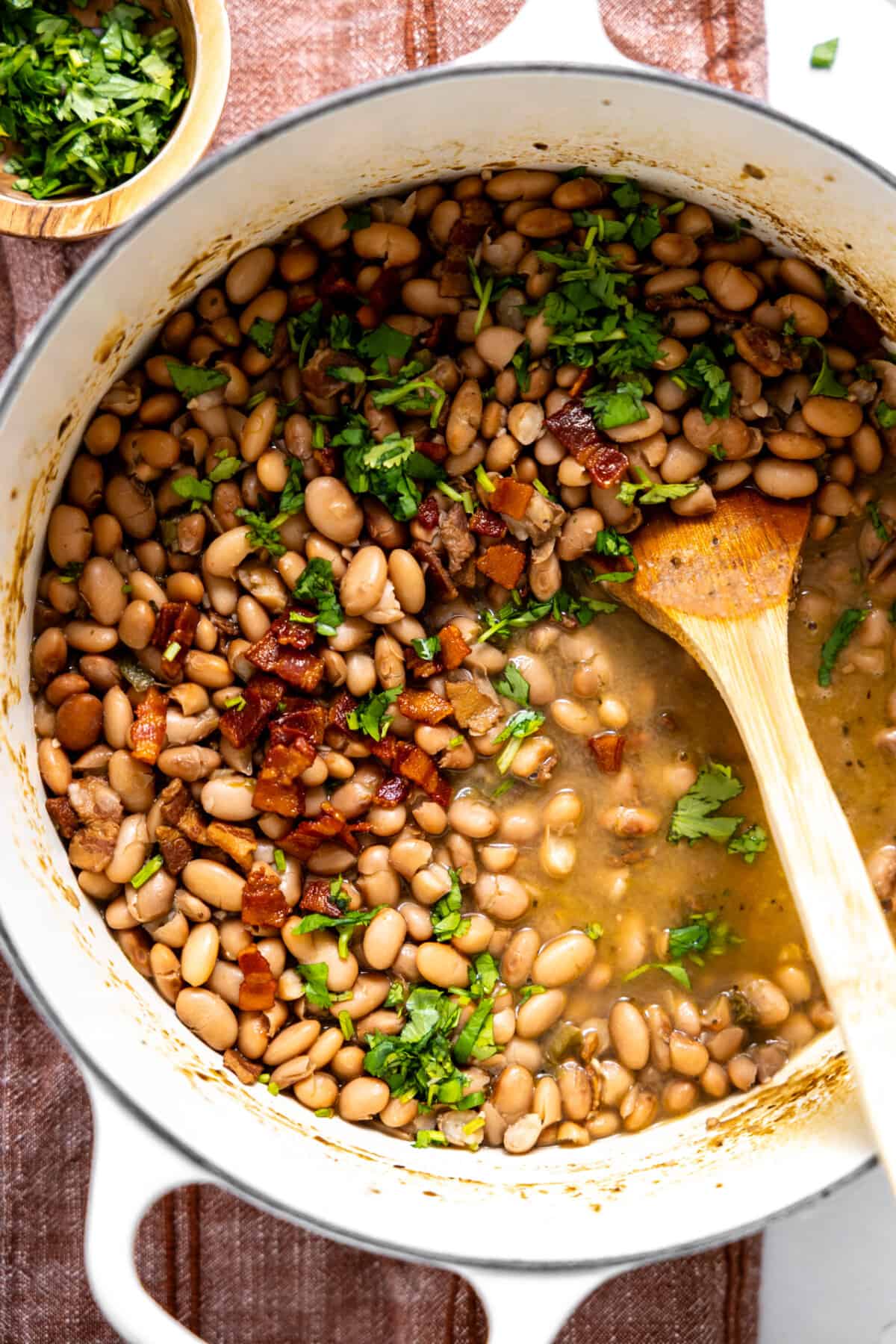 Pot of charro beans topped with cilantro and crispy bacon.