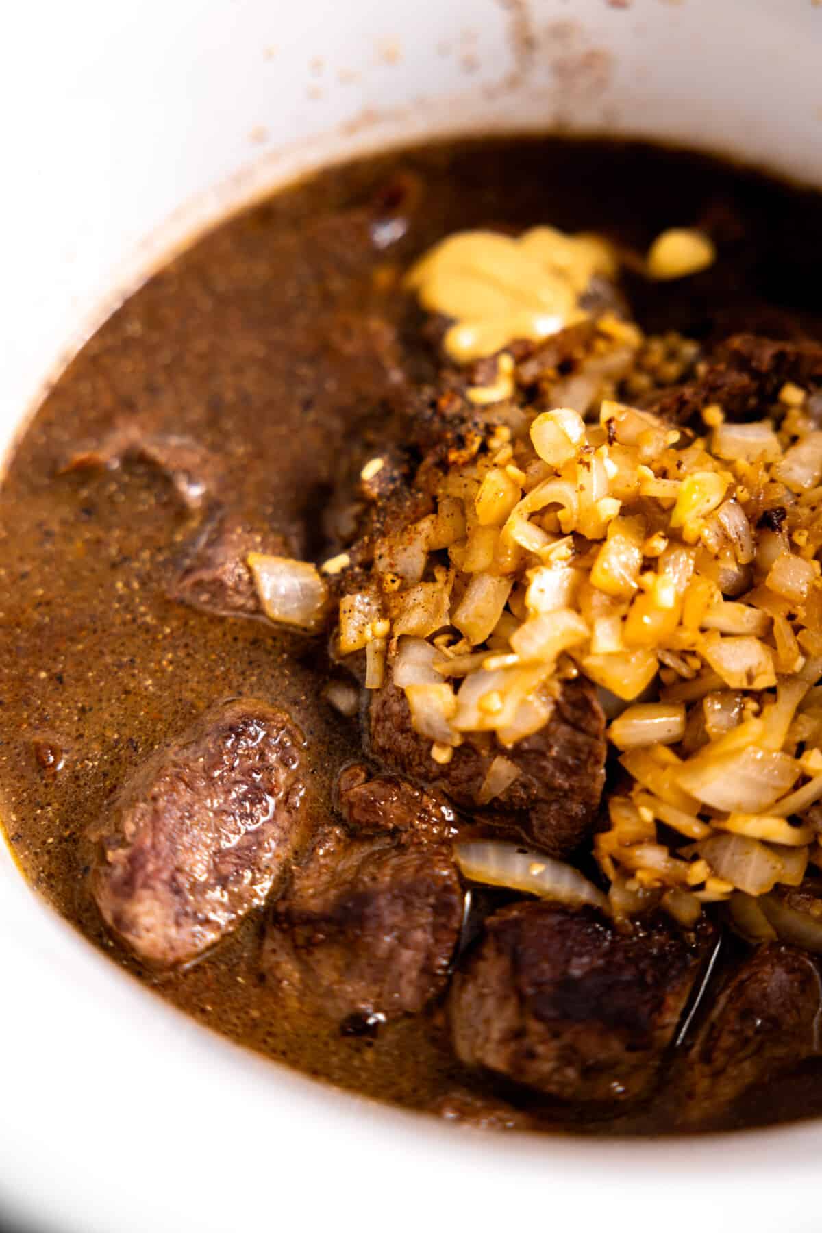 Seared beef in broth with onions and garlic added to slow cooker.
