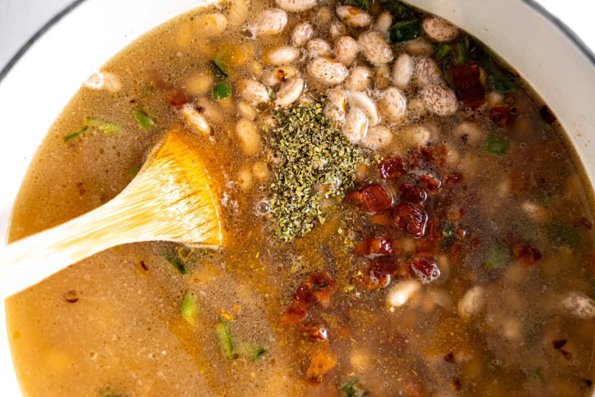 Dutch oven filled with broth, pinto beans, bacon, and seasonings.