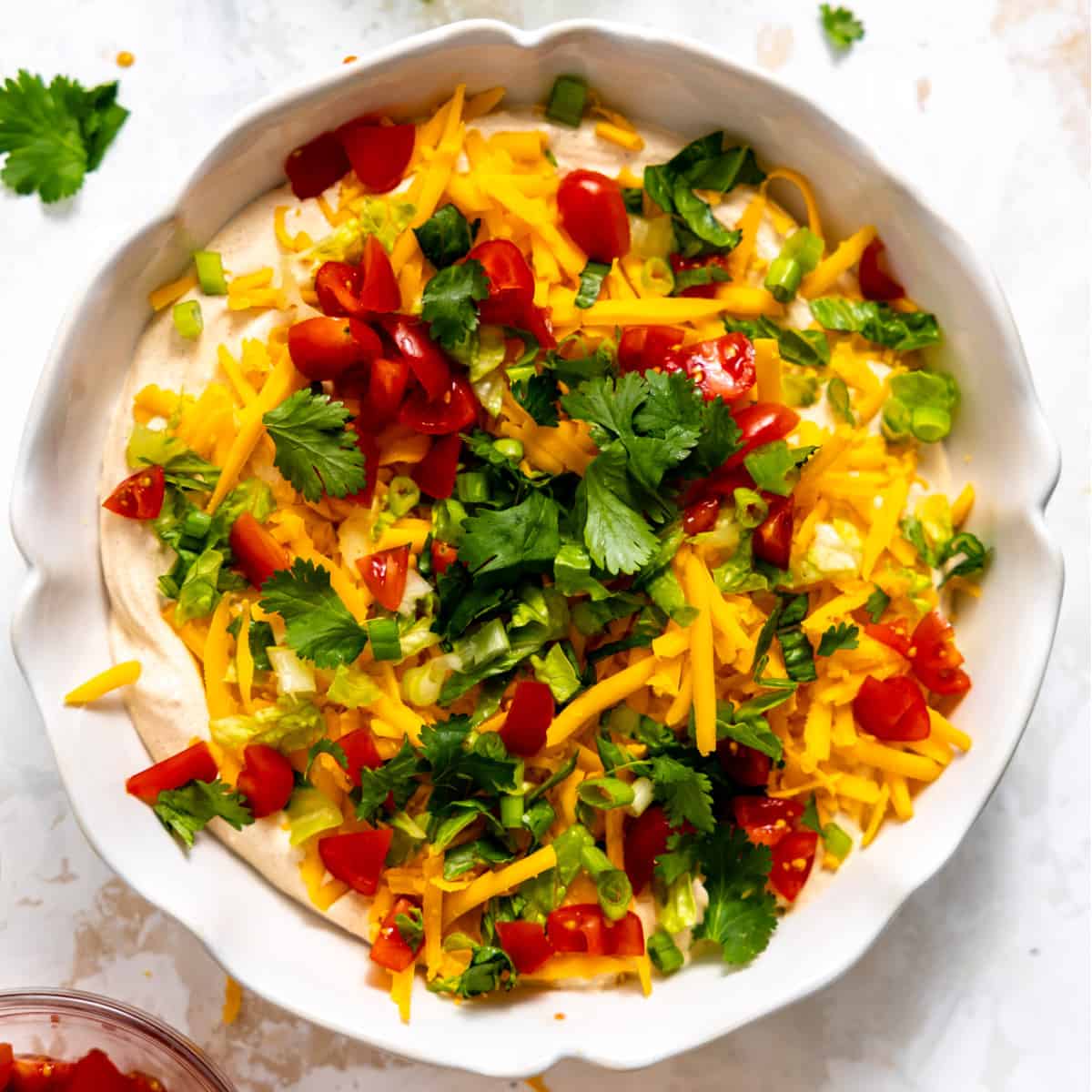 Taco dip topped with fresh taco toppings in a white serving dish. 
