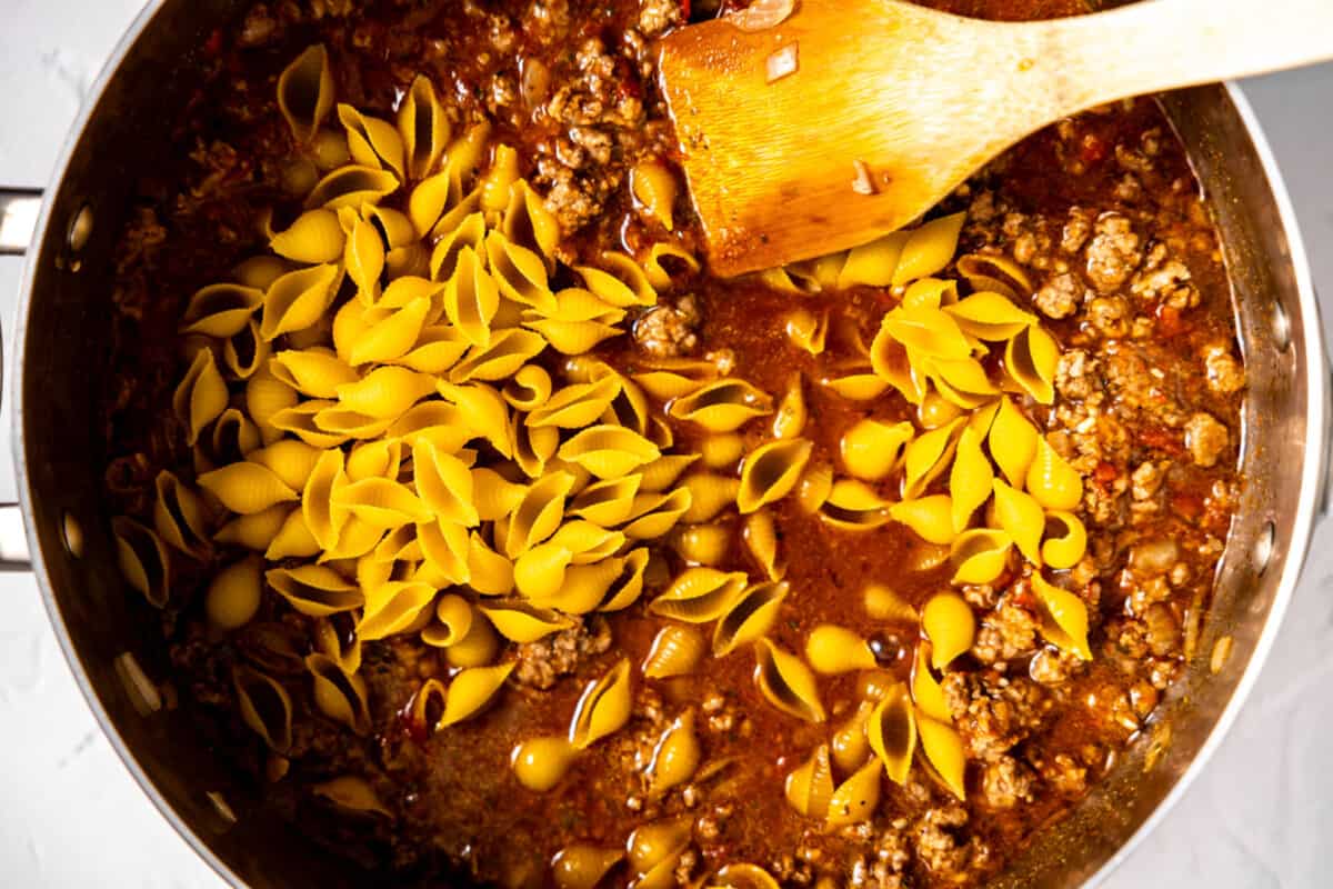 Skillet with ground beef, sauce and shell noodles.