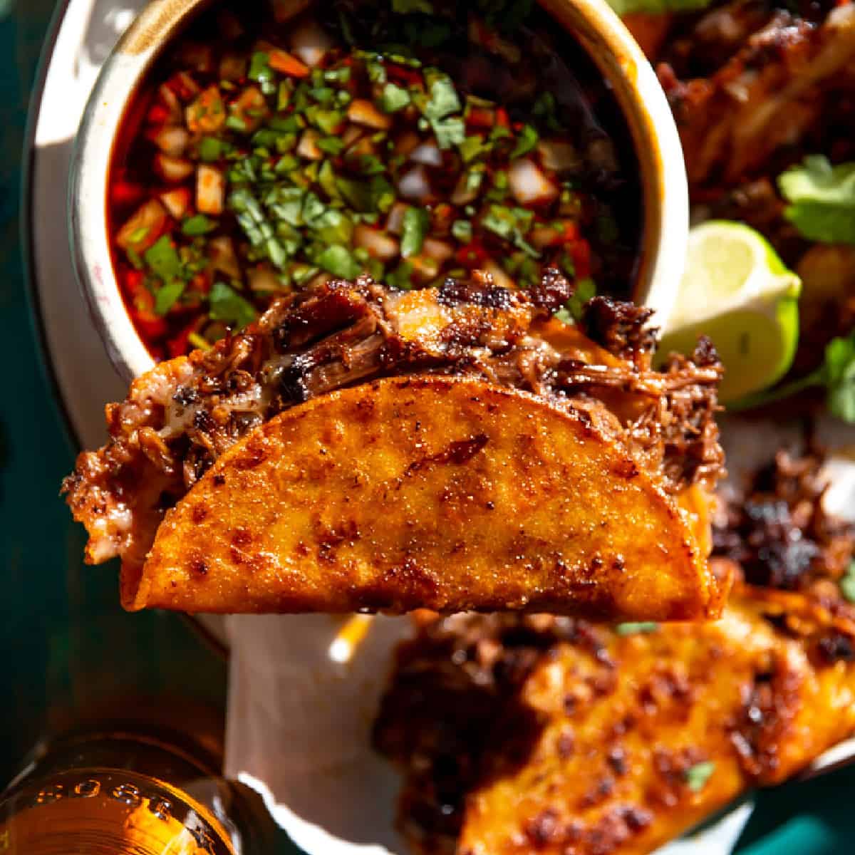 Birria taco balancing on a bowl of consommé.