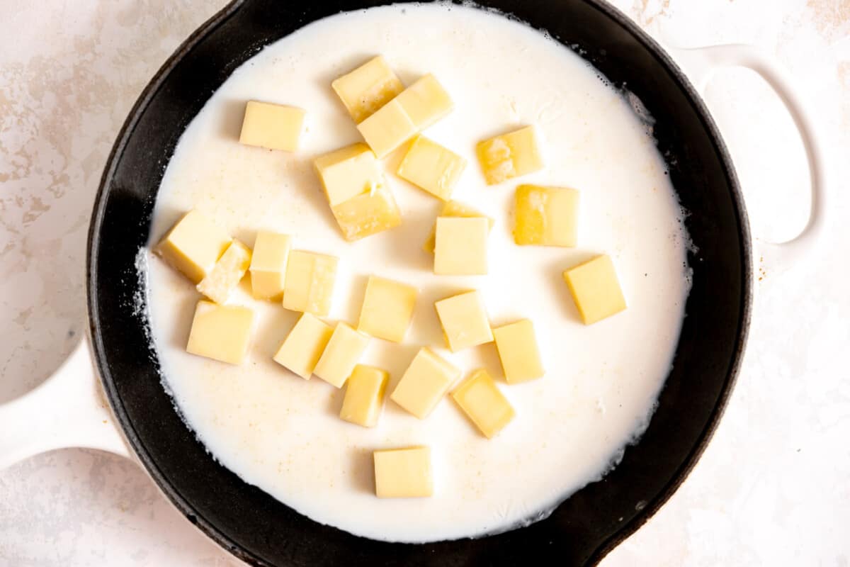 Skillet with cream and chunks of white American cheese melting. 