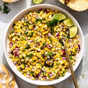 Bowl of roasted corn salsa with lime wedges.