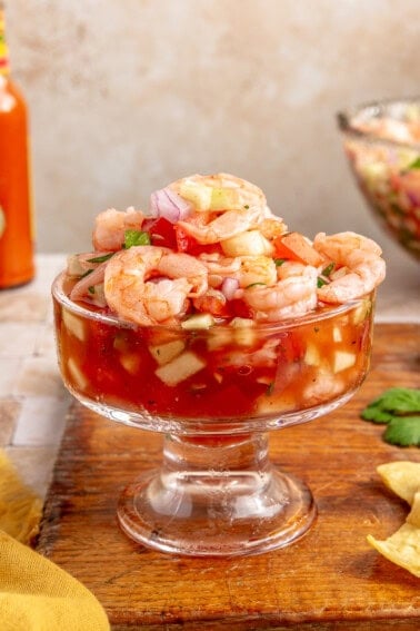 Mexican shrimp cocktail served in a glass cocktail glass on a wood board.