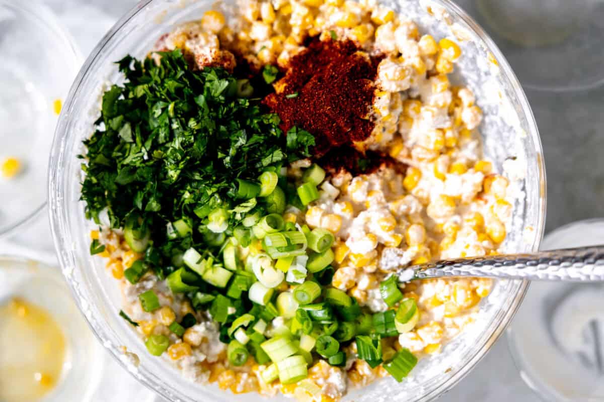 Adding diced green onion, chopped cilantro, and chili powder to make Mexican corn dip.