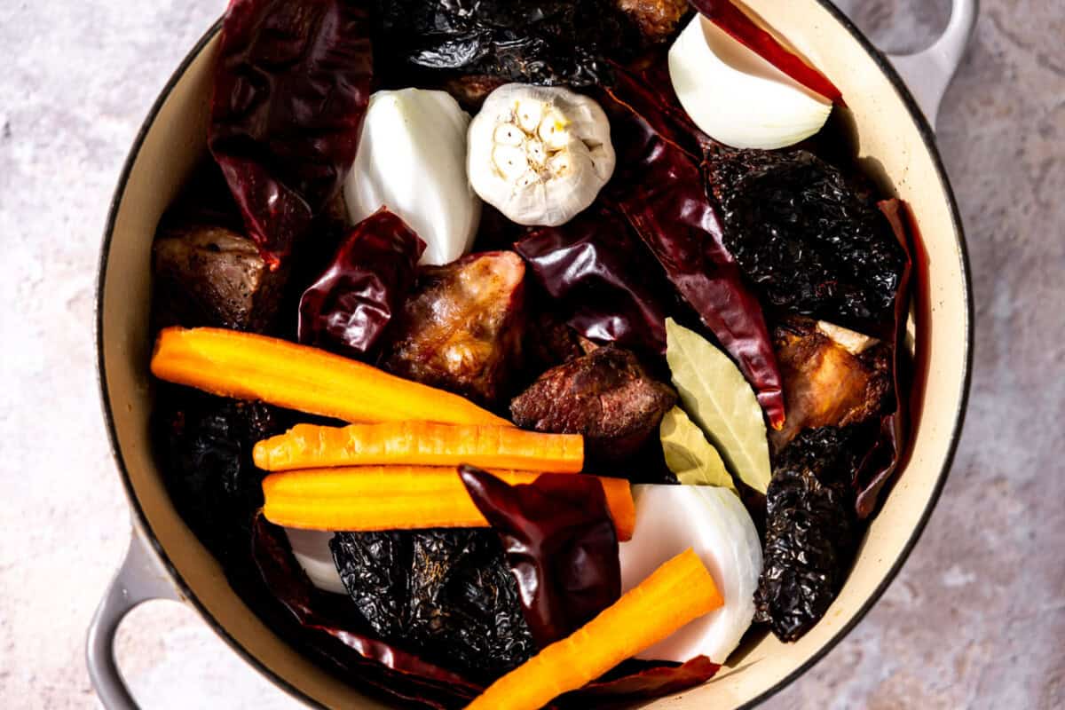 Large dutch oven with beef, Chile peppers, onion, garlic, carrots, bayleaves, water and seasonings. 