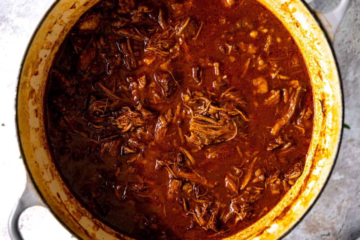 Large dutch oven filled with cooked birria after shredding the meat.