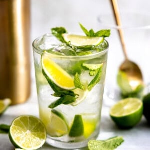 Glass with mojito with fresh mint and lime wedges.