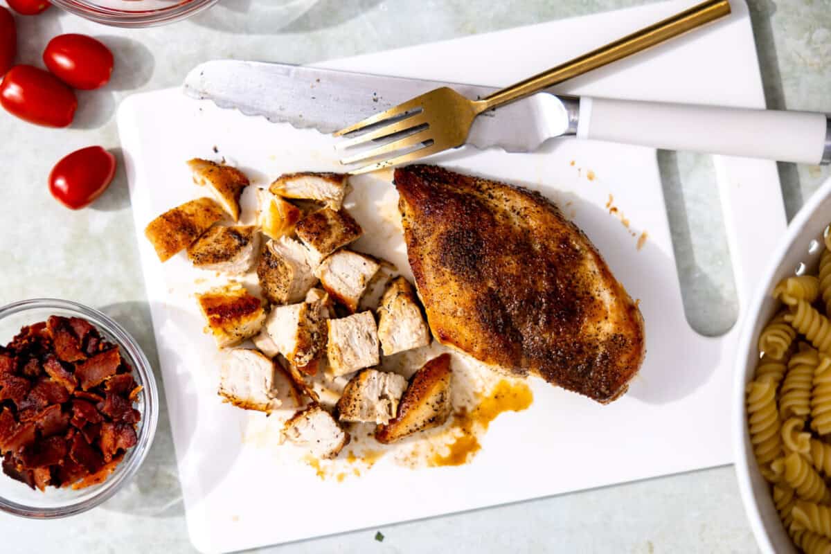 Cooked chicken breast being chopped for pasta salad. 