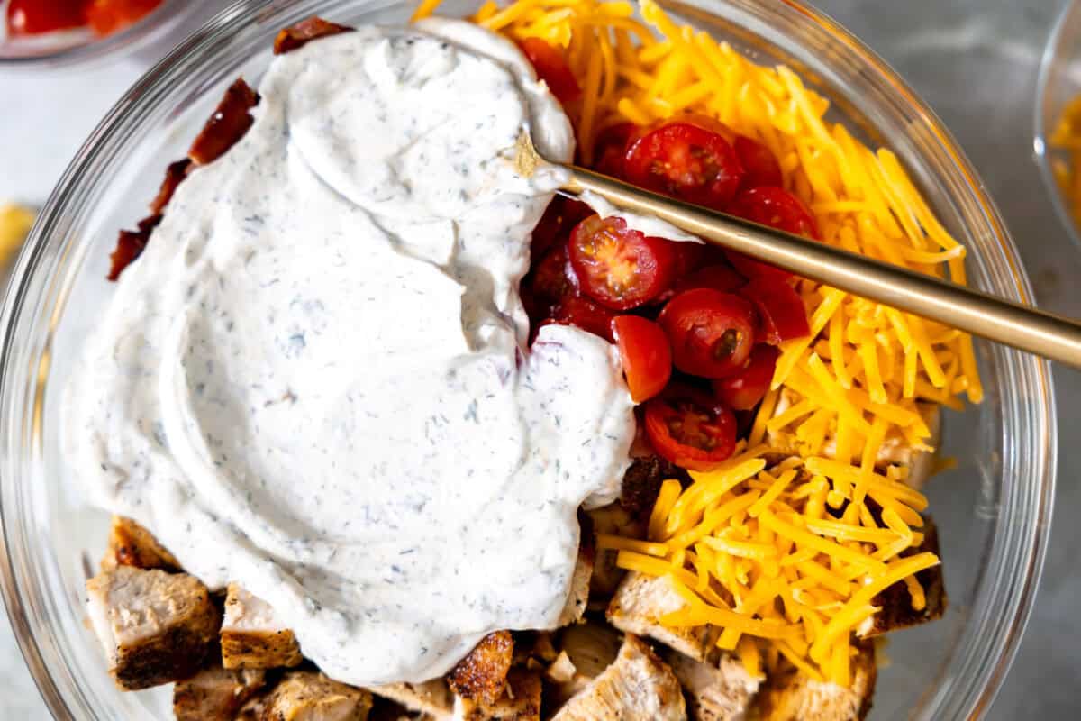 Ranch dressing being added to pasta salad.