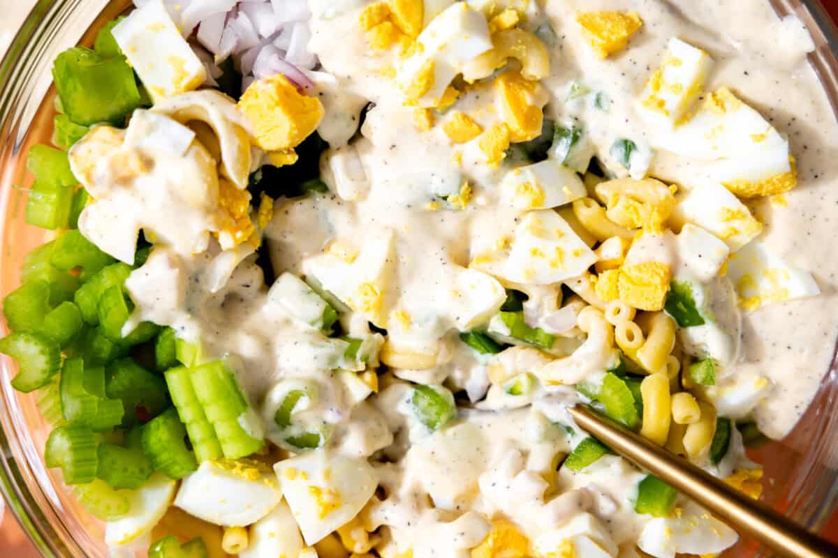 Dressing being added to a bowl of macaroni salad. 