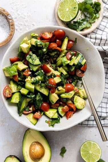 Bowl with avocado tomato and cucumber salad with a cilantro lime vinaigrette.