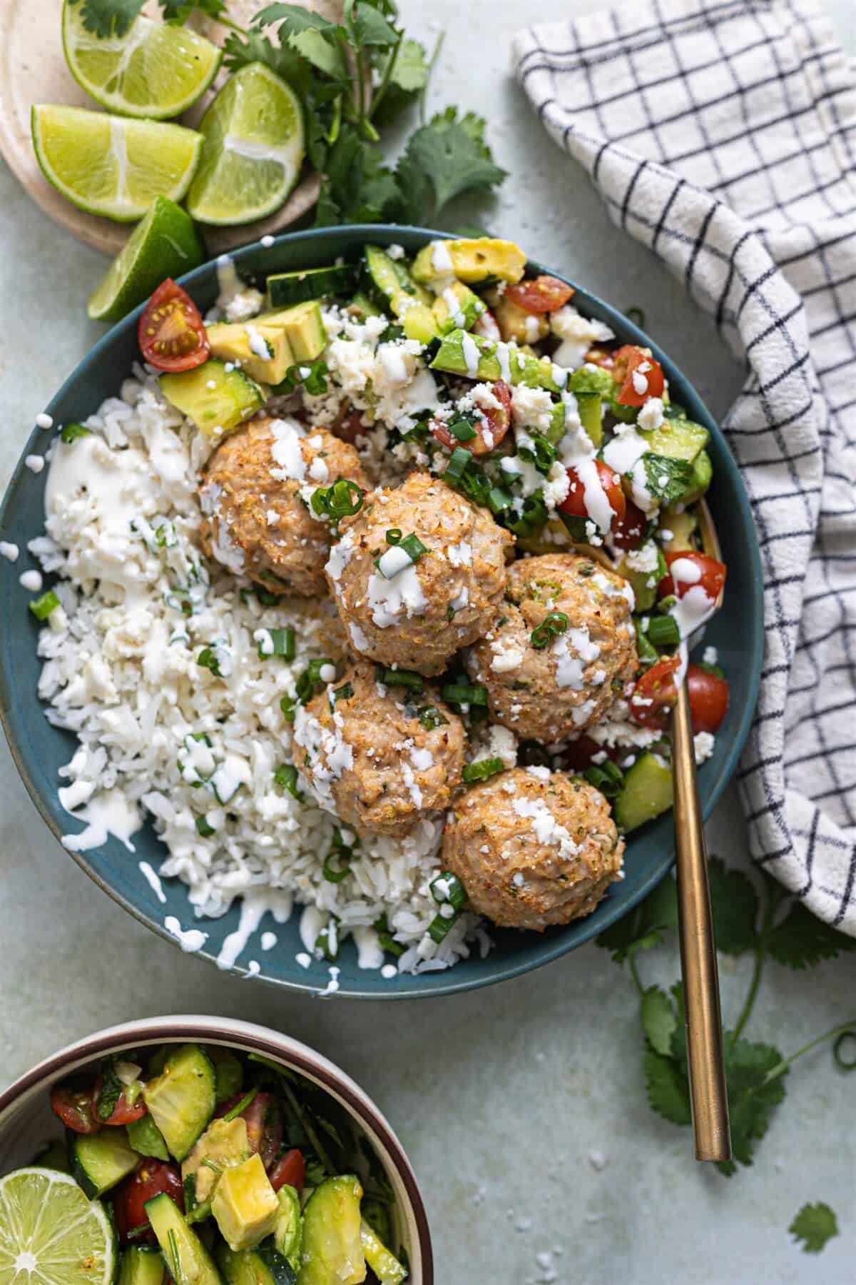 Bowl of rice, cilantro lime chicken meatballs and tomato avocado salad drizzled with crema and crumbled queso fresco. 
