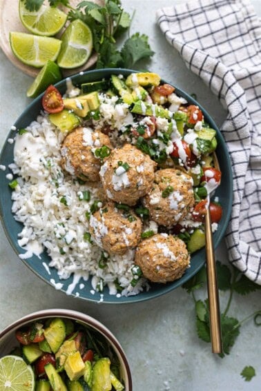 Bowl of rice, cilantro lime chicken meatballs and tomato avocado salad drizzled with crema and crumbled queso fresco.