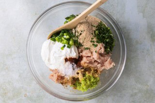 Ground chicken and ingredients needed to make meatballs in a glass bowl.