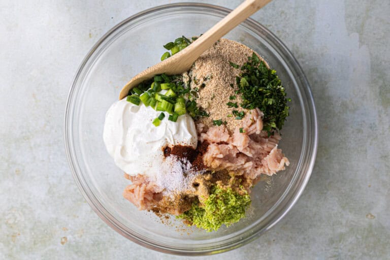 Ground chicken and ingredients needed to make meatballs in a glass bowl.