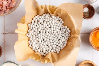 Pie dish with crust lined with parchment paper and filled with pie weights.