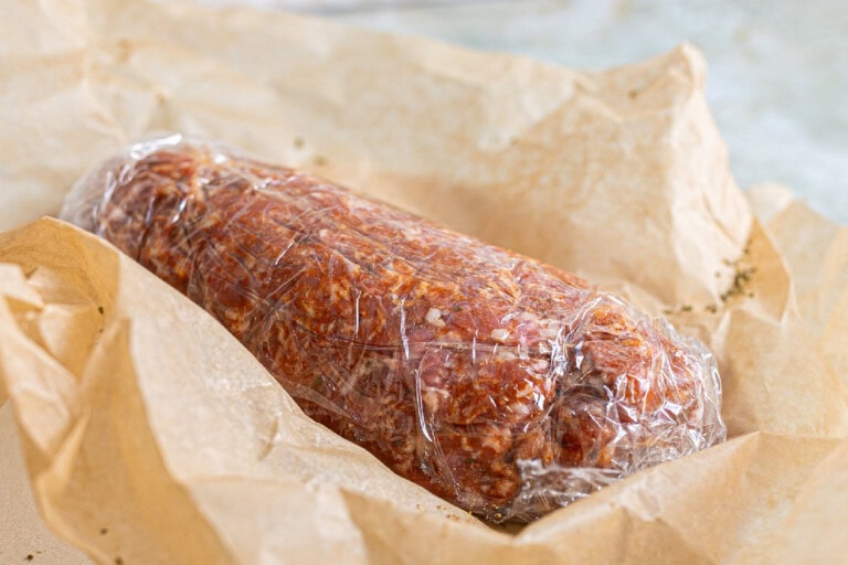 Chorizo wrapped in plastic sitting on top of a brown paper